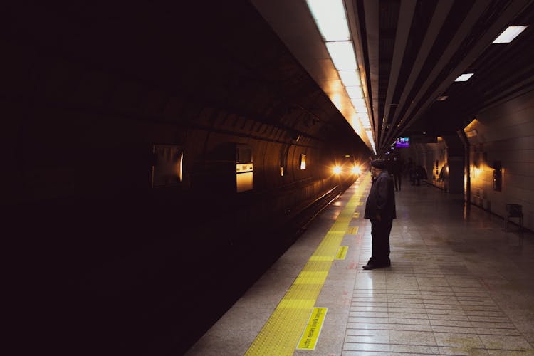 Man In Black Jacket Standing Behind The Yellow Line While Waiting For The Train 