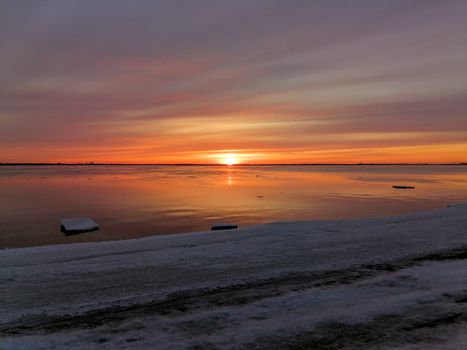 Stunning sunset reflecting on a still, partially frozen lake, creating a serene winter landscape.
