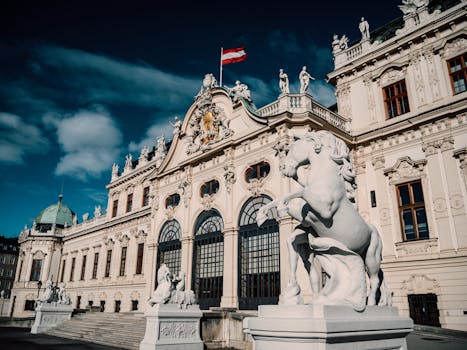 A magnificent Baroque palace in Vienna, Austria, adorned with sculptures and the national flag under a vivid blue sky.