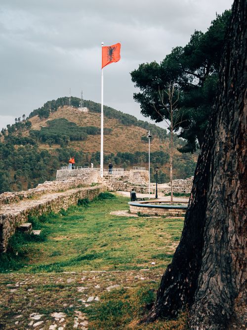 Free Albanian flag waves proudly at a historic fortress amid lush hillside views. Stock Photo