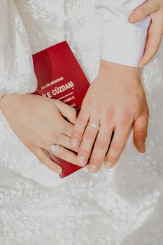 A close-up photo capturing a couple's hands displaying wedding rings and a marriage document.