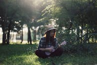 一名妇女坐在阳光明媚的公园树下，弹着尤克里里，享受着平静的时光