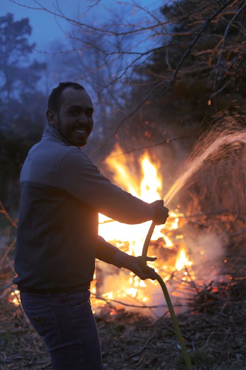 Free A Man Smiling Holding a Water Hose Extinguishing Fire Stock Photo