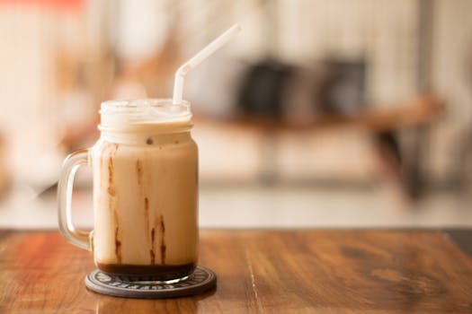 Close-up of iced coffee in a mason jar on a wooden table, perfect for a café vibe., Photographer: Archie Binamira