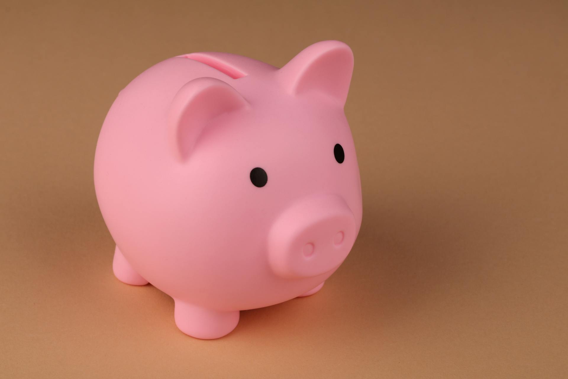 A pink piggy bank symbolizes savings and budgeting on a simple brown backdrop.