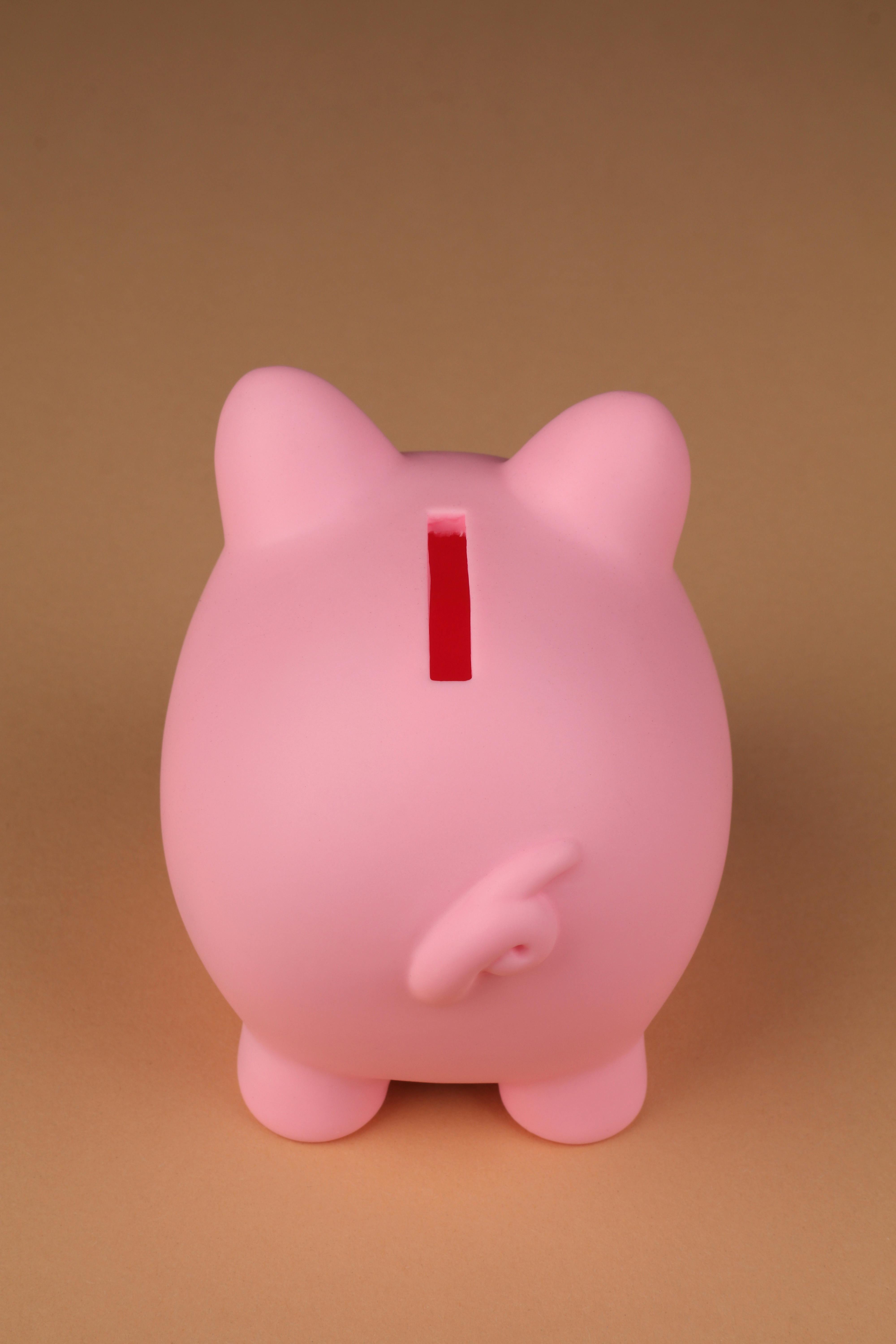 Pink piggy bank standing on a neutral brown surface, captured in a minimalist style.