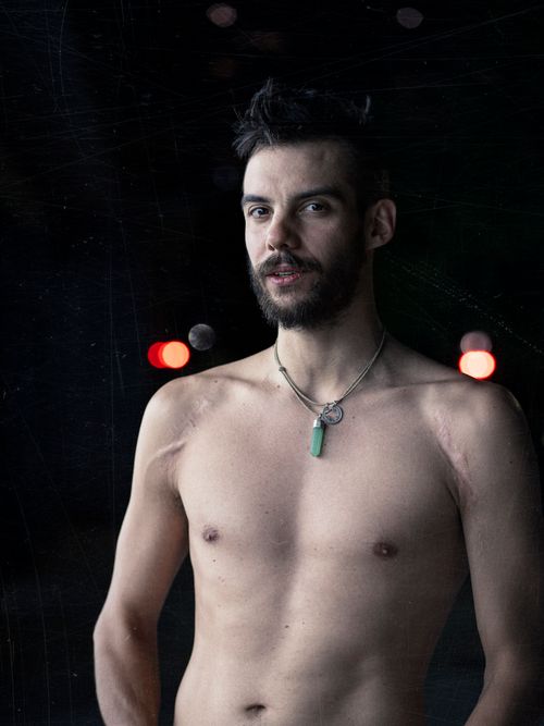 Free Portrait of a bearded man, shirtless, wearing a necklace against a dark background with bokeh lights. Stock Photo