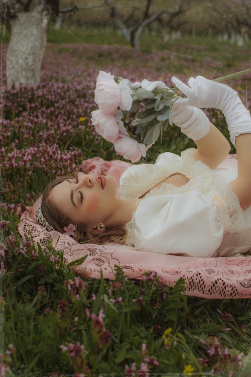 Free Woman in White Dress Lying on Pink Lace Textile in a Flower Garden Stock Photo