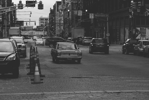 Black and white street view with vintage and modern cars on an urban road.