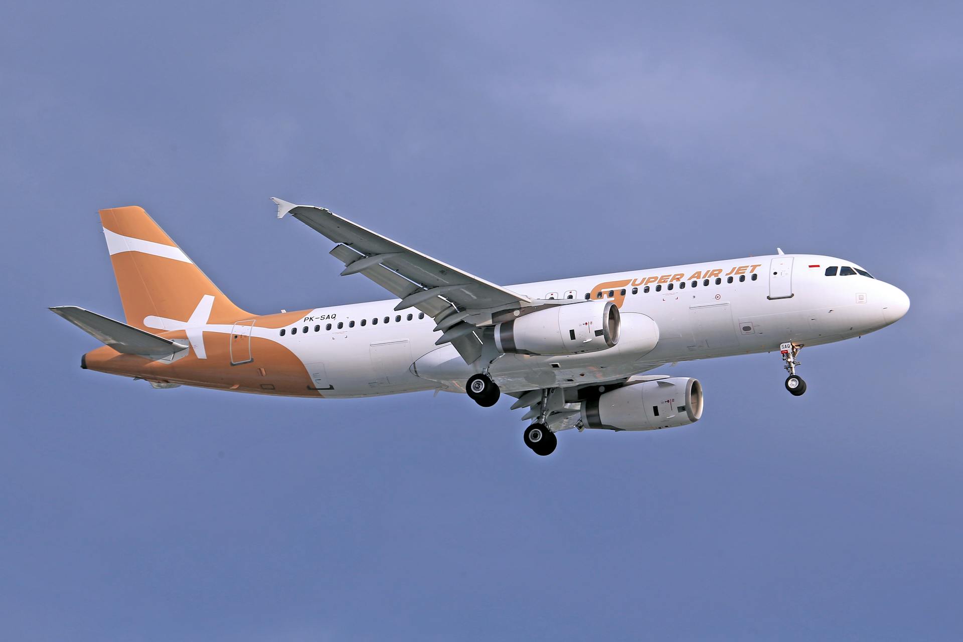 A commercial airplane with orange and white livery flying high against a clear blue sky.