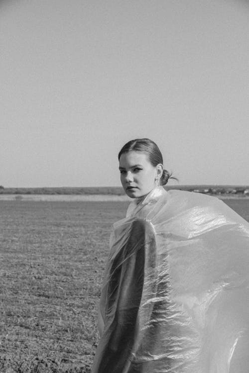 A Woman Covered with Transparent Plastic Standing on a Grass Field while Looking at the Camera