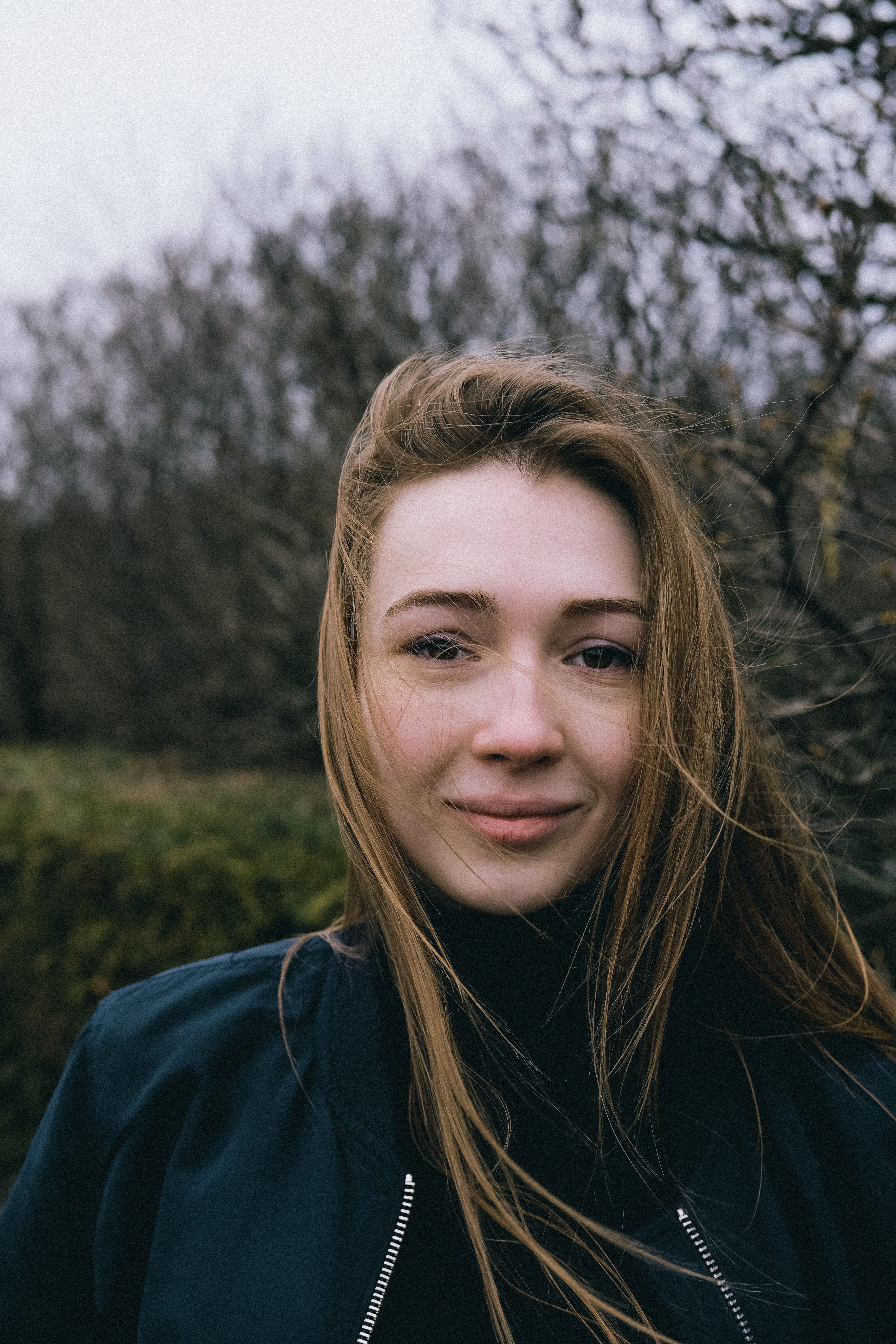 Portrait of a young woman with tousled hair standing outdoors on a windy day.