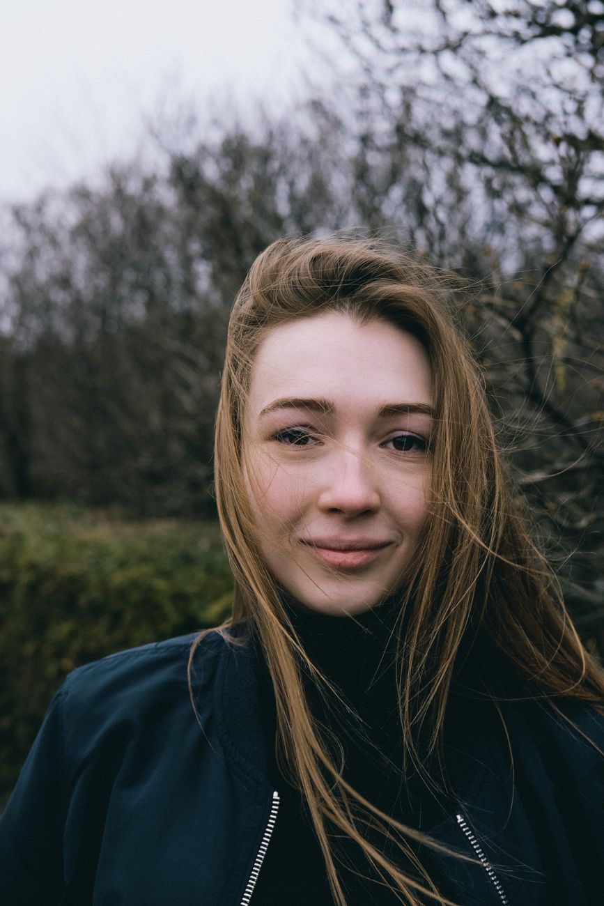 Portrait of a young woman with tousled hair standing outdoors on a windy day.