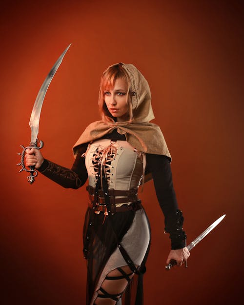 Woman in Brown Warrior Costume Holding  Sword and Dagger