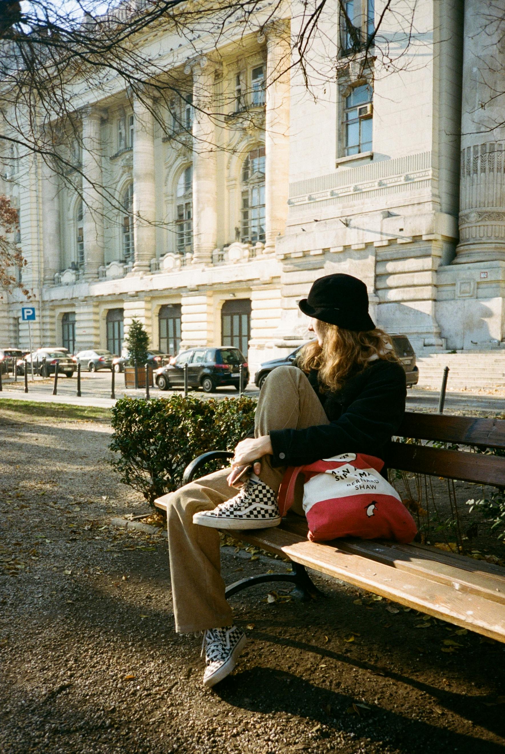 Casual scene of a young woman in Budapest sitting on a bench with a backpack.