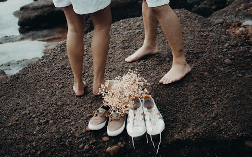 Free Couple Standing Barefoot on Beach with Bouquet Lying on Their Shoes Stock Photo