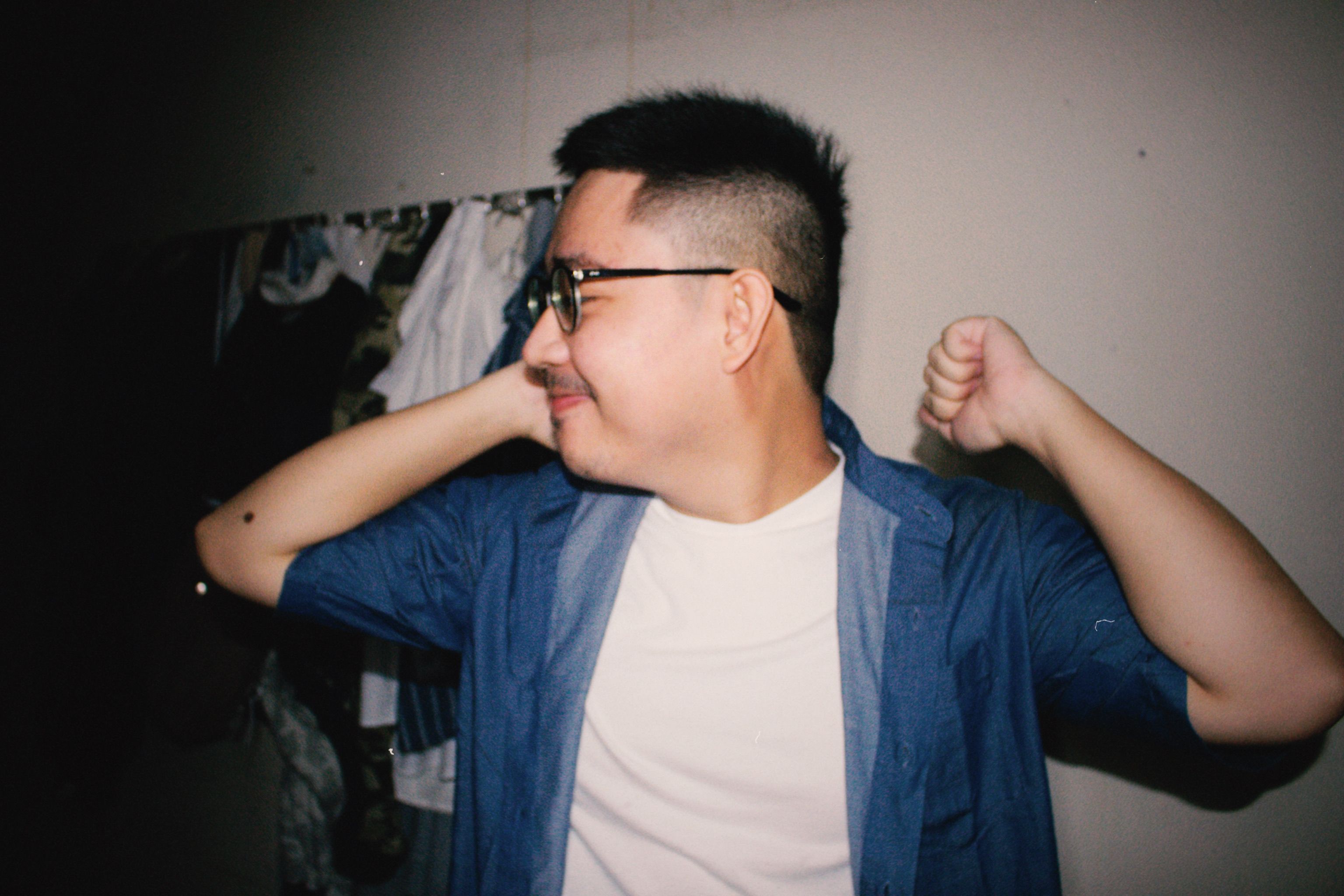 Happy Asian man in denim shirt and eyeglasses smiling and relaxing indoors.