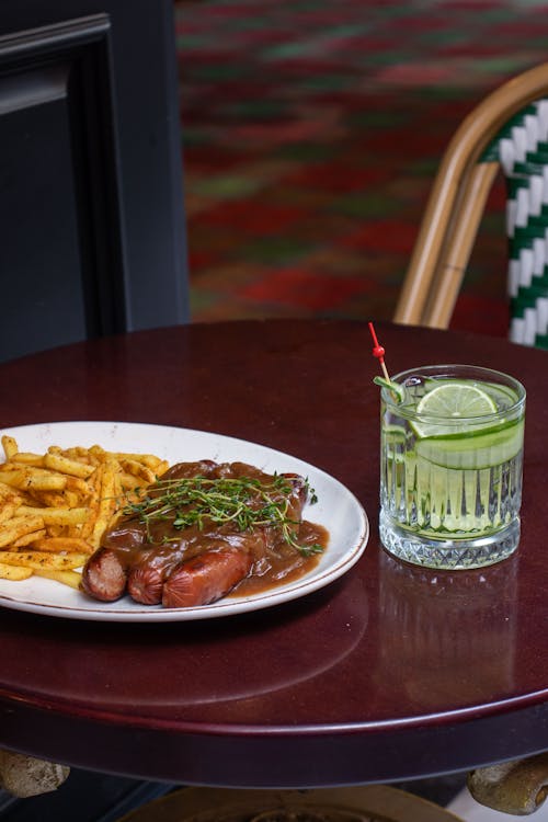 Sausages With Gravy and French Fries Near a Glass of Drink