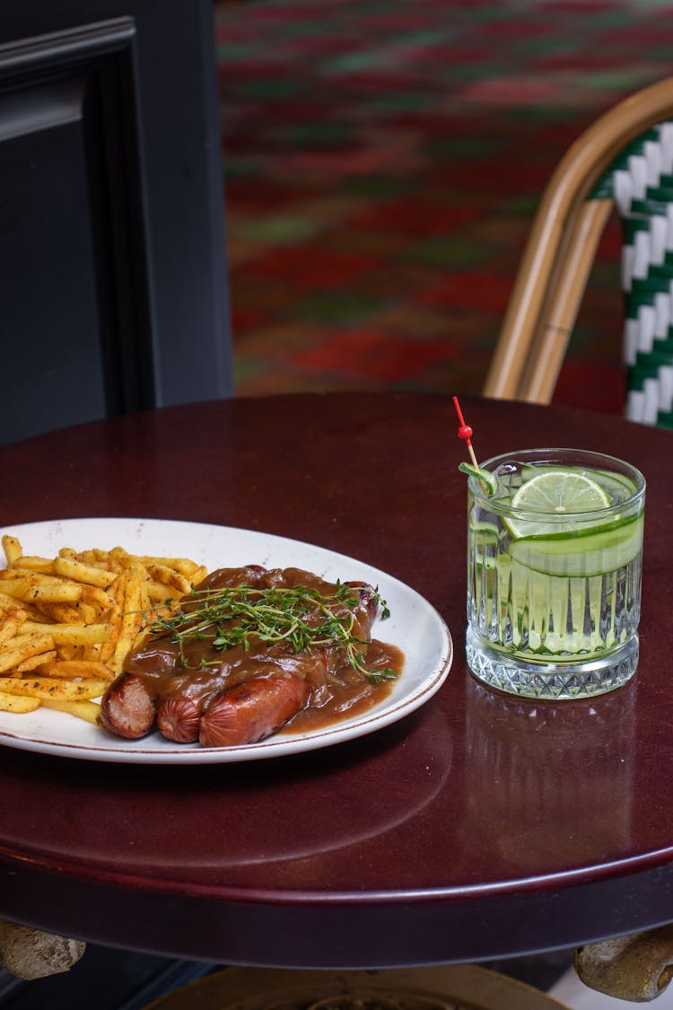 Sausages With Gravy And French Fries Near A Glass Of Drink