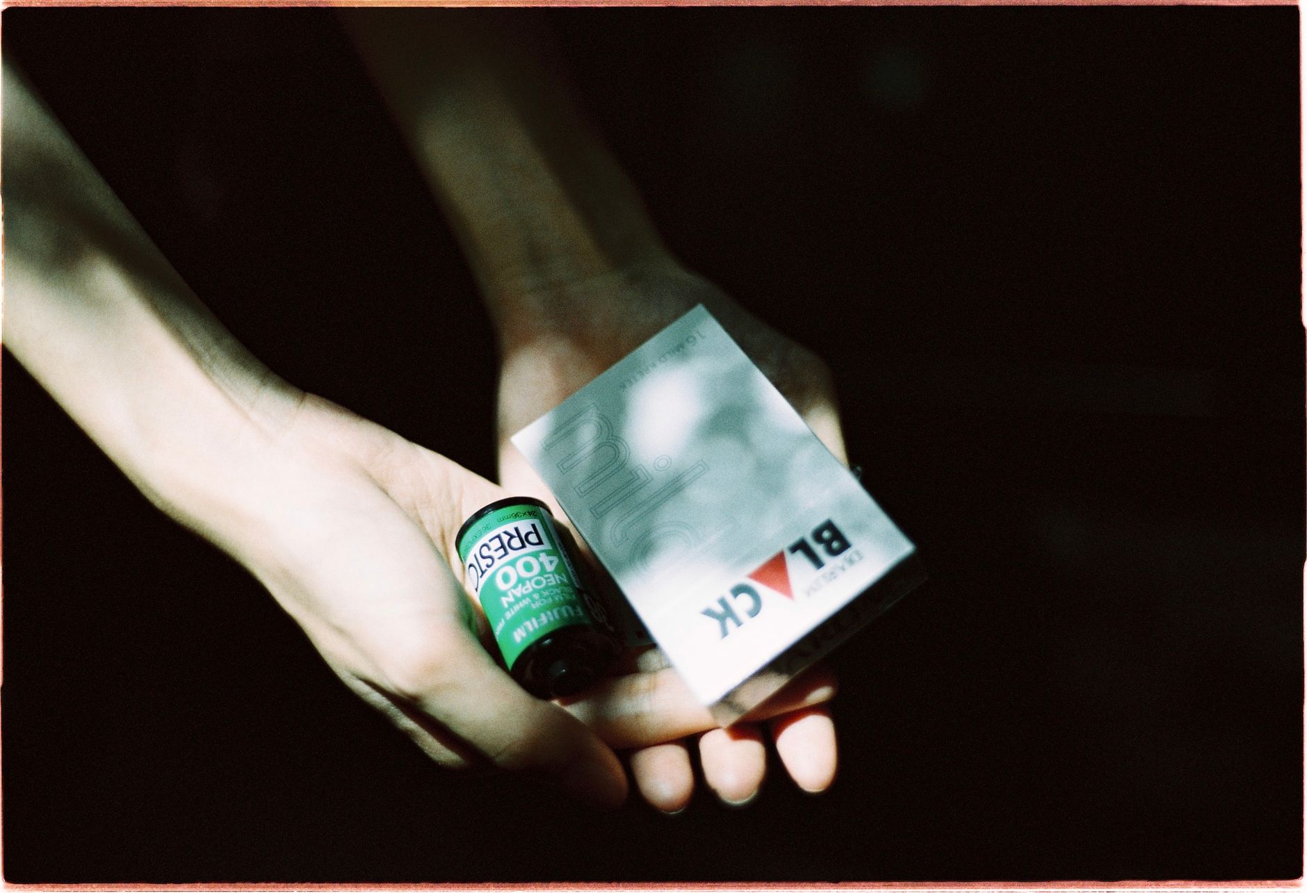 Close-up of hands holding a film roll and cigarette box in moody lighting.