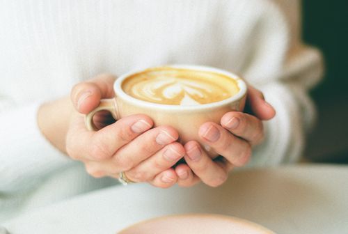 Free Close-up of hands holding a warm cappuccino cup with latte art in a cozy indoor setting. Stock Photo