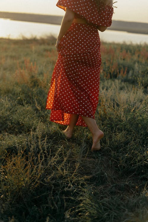 Woman in Red and White Polka Dot Dress Walking on Green Grass Field