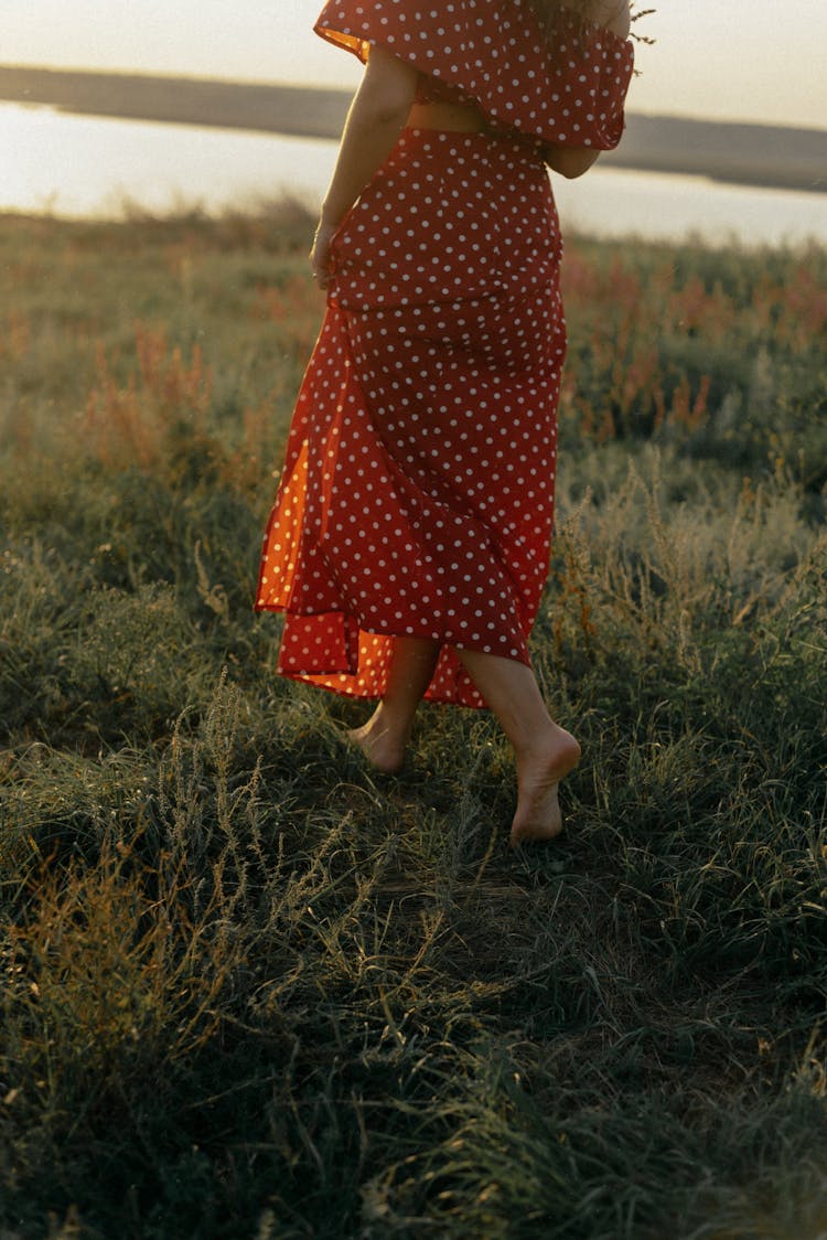 Unrecognizable Woman In Red Summer Dress Walking Barefoot In Meadow