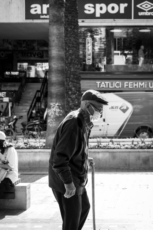 Free Senior man in mask and black jacket using cane on urban street. Stock Photo