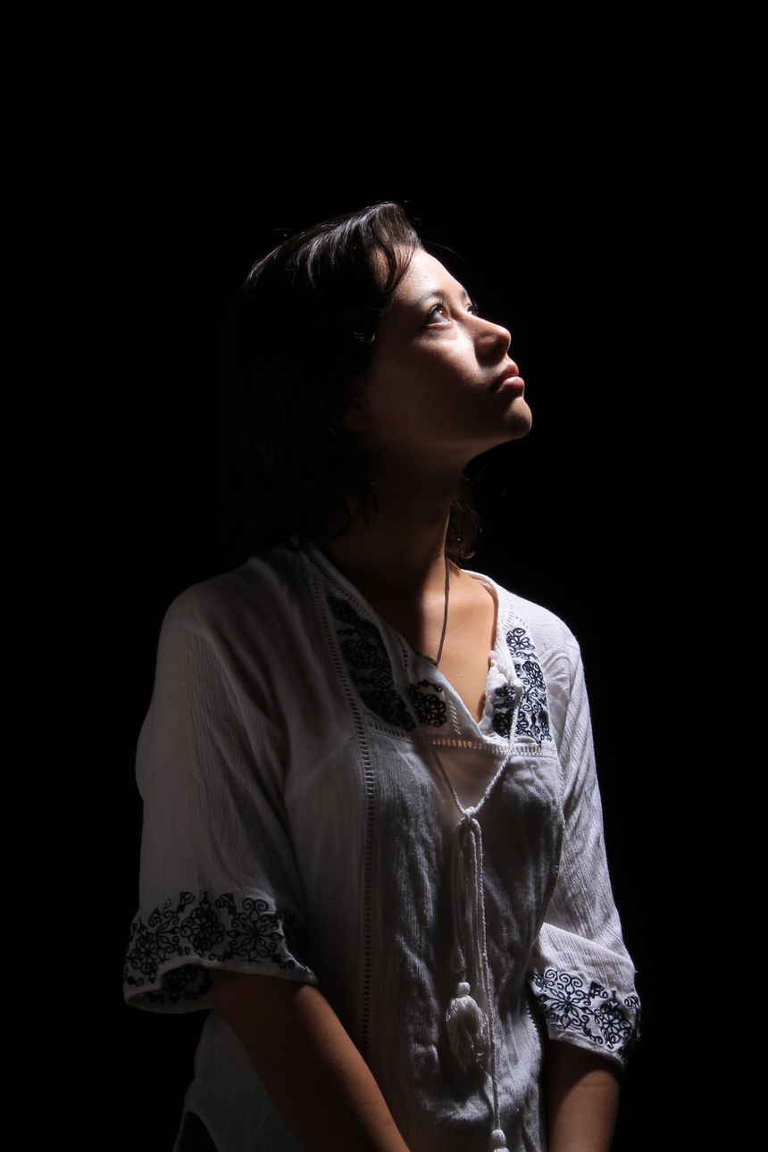 Studio portrait of a woman looking upward against a dark background, photo by vics ilustrada on Pexels