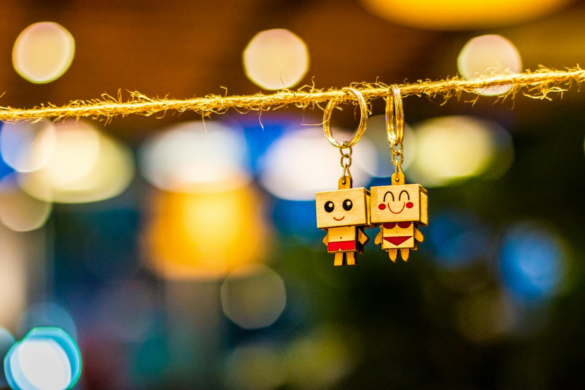 Two Man and Woman Wooden Couple Keychains Hanging on Rope Overlooking Bokeh Lights