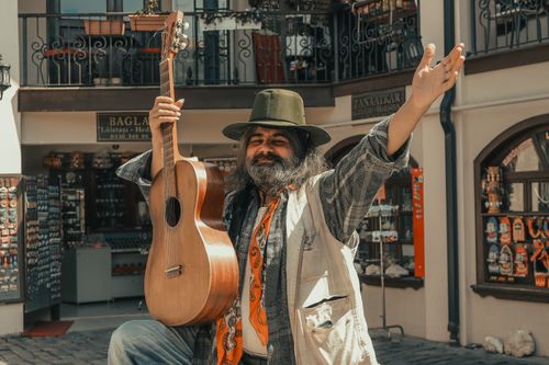 Free Bearded man in hat performing with guitar in a vibrant outdoor market. Stock Photo