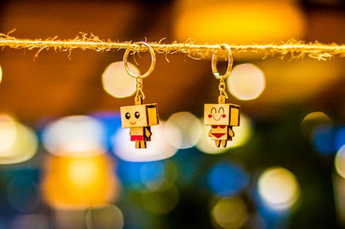 Free Two Brown Wooden Character Keychains Hanged on Brown Rope Stock Photo