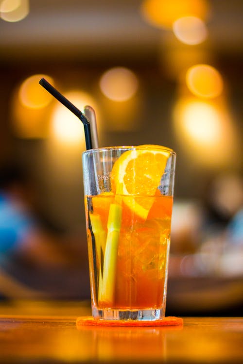 Прозрачный стакан для питья, наполненный апельсиновым соком с черной соломинкой