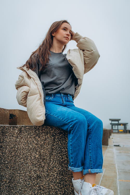 A Woman in Denim Jeans Sitting on a Concrete Surface