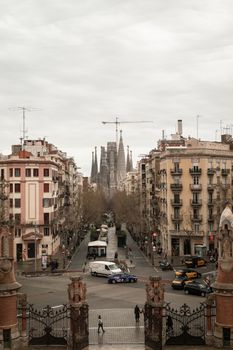 Urban view of Sagrada Familia from a busy Barcelona street on an overcast day.