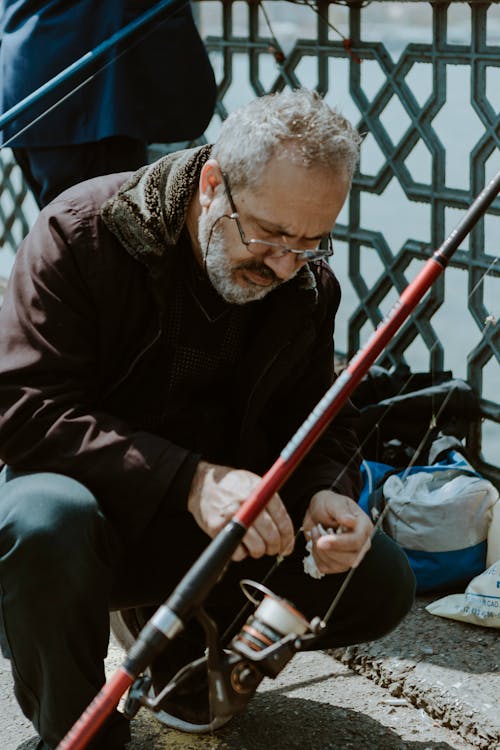 Man in Brown Jacket and Black Pants Beside a Fishing Rod