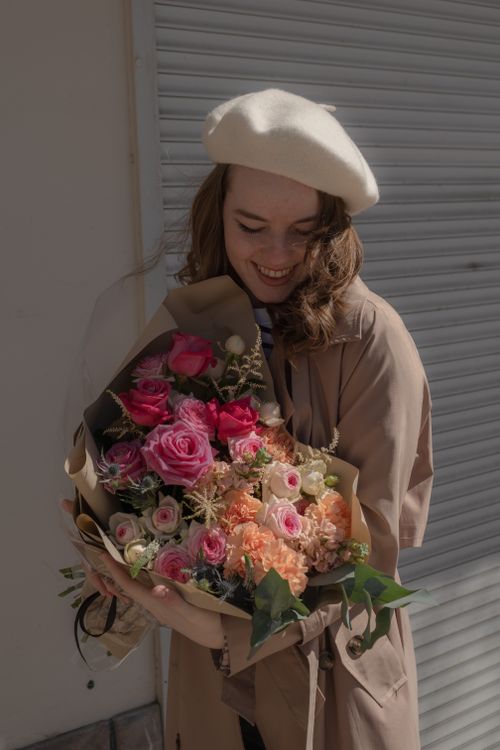 Free Young woman in a beret holding a vibrant bouquet of flowers, smiling warmly in soft light. Stock Photo