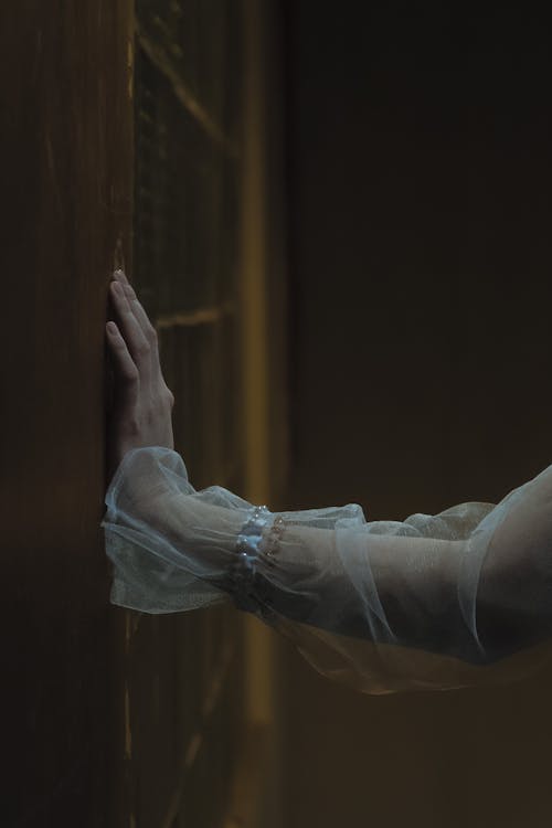 Темное эстетическое фото девушки, одетой в белое платье и трогающей старую стену