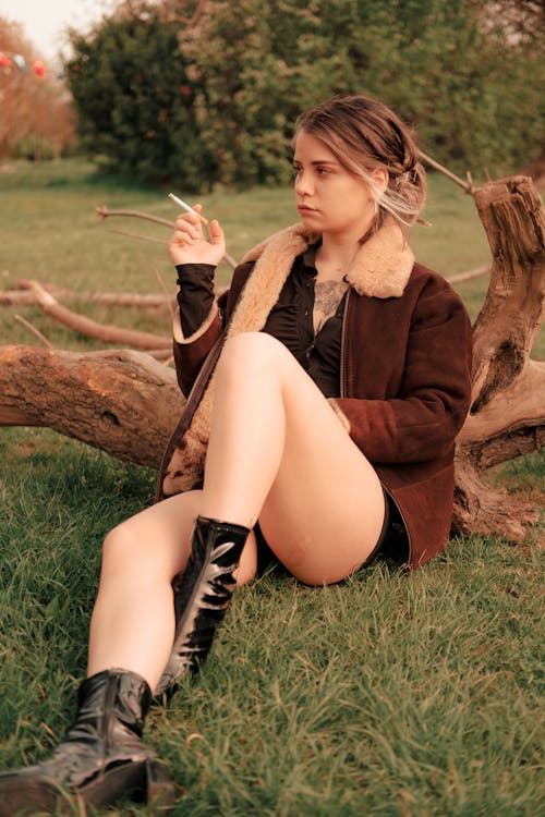 Woman in Brown Coat Sitting on a Grassy Field
