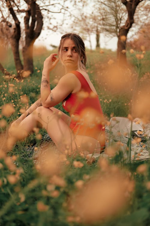 A Woman in Red Bodysuit Sitting on Green Grass Field