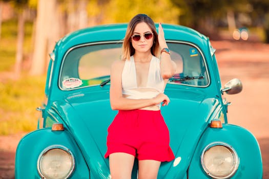 Fashionable woman in sunglasses leaning on a classic turquoise VW Beetle outdoors.