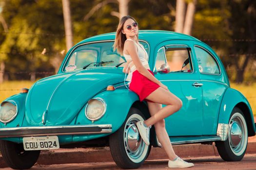 Woman posing with a vintage turquoise Volkswagen Beetle, embracing retro style outdoors.