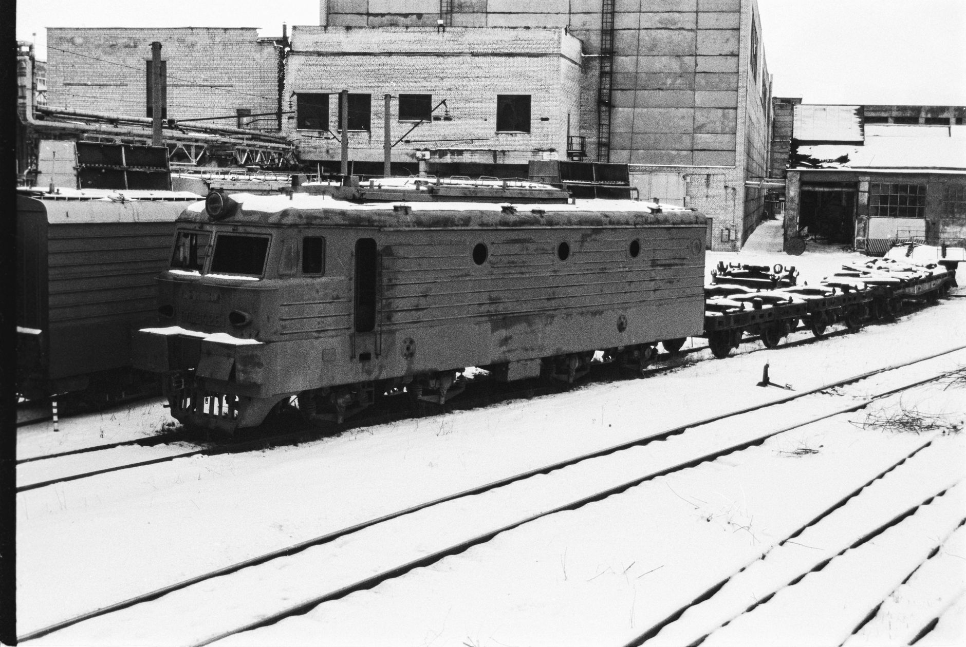 Black and white photo of a vintage train locomotive in a snowy industrial area, Lviv, Ukraine.