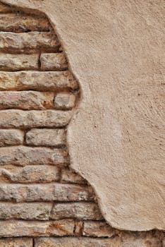 Close-up of a weathered brick wall partially covered with rough plaster.