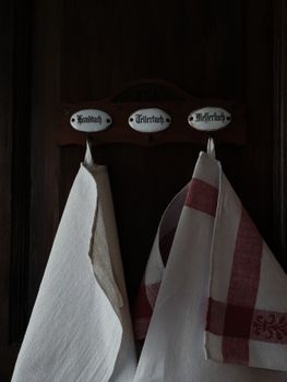 Two kitchen towels hanging on rustic wooden hooks labeled in German, evoking a nostalgic feel.