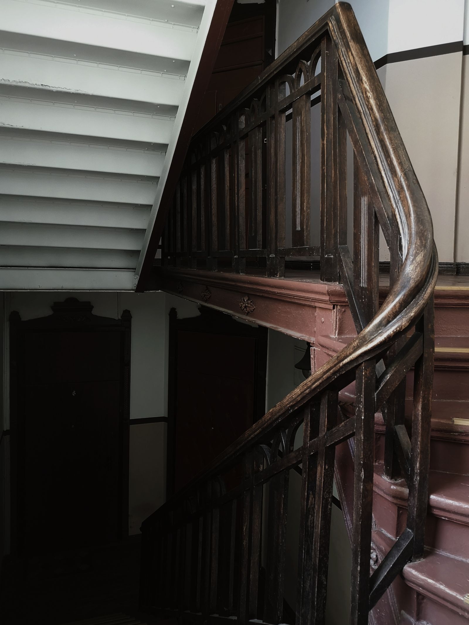 Escalier en bois ancien à rampe ouvragée, marches creusées par l'usage, dans une cage d'immeuble