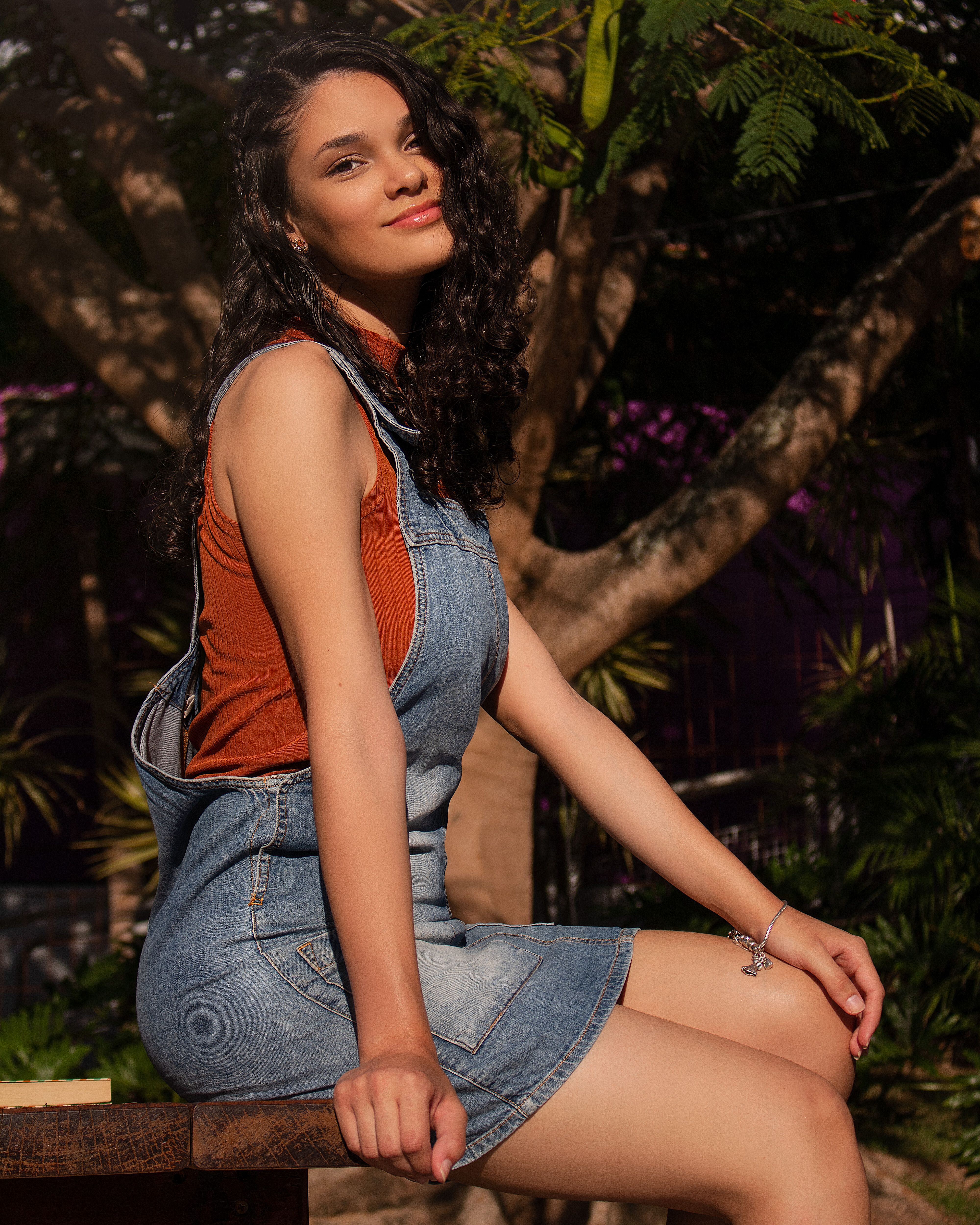 Woman in a denim jumper sitting outdoors, smiling under the sunlight