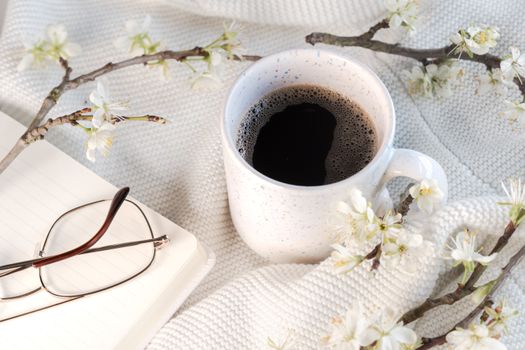 A serene cup of coffee surrounded by spring blossoms on a textured surface.