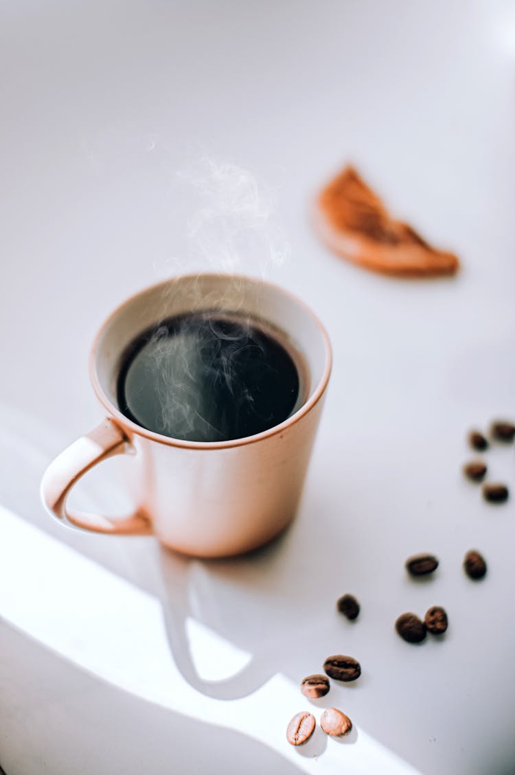 Steaming Cup Of Coffee With Coffee Beans