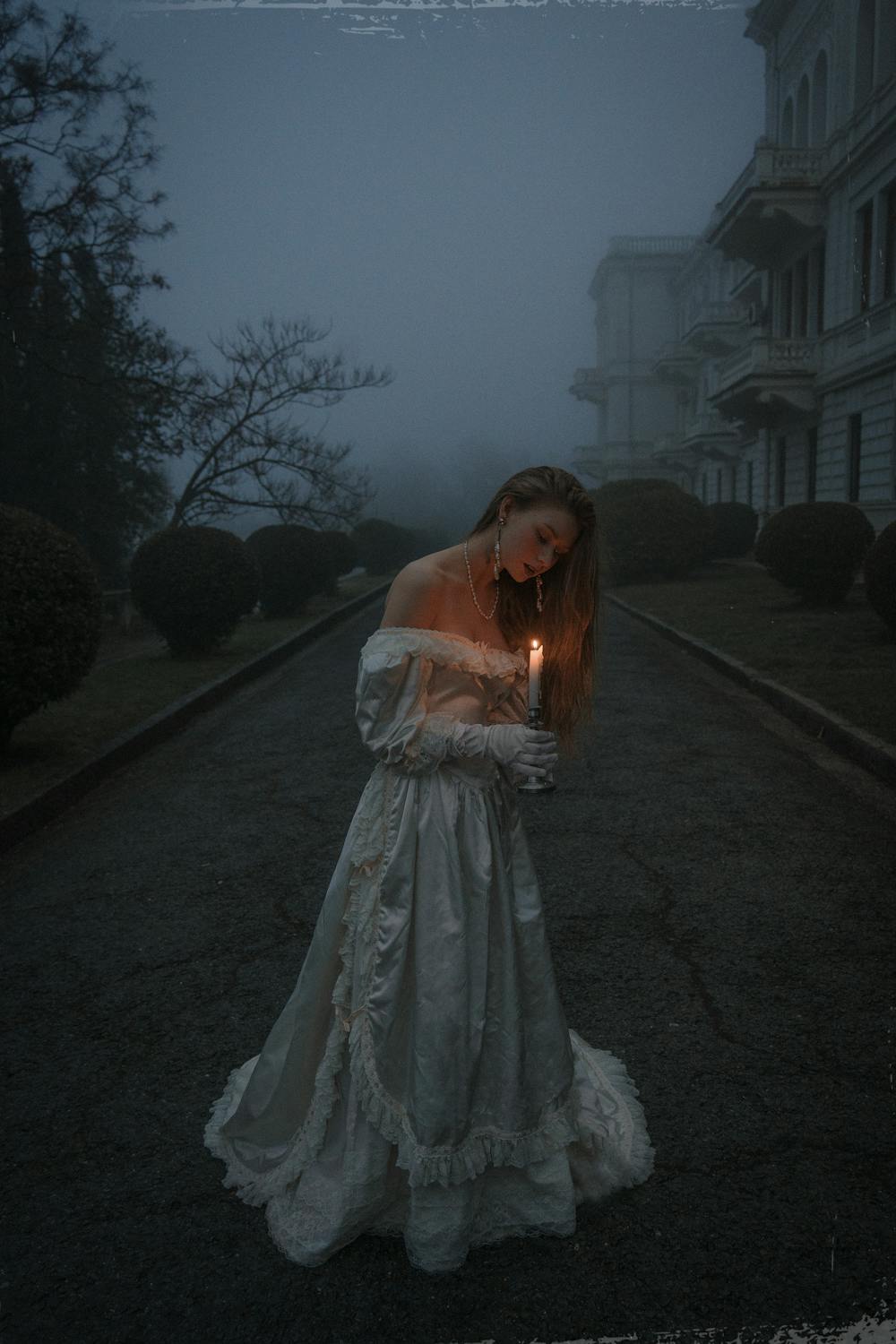 Woman in a Long Vintage Dress Holding a Lit Candle Outside in Fog ...